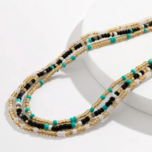 Detailopname van de drielaagse tailleketting met gouden, zwarte en turquoise kralen