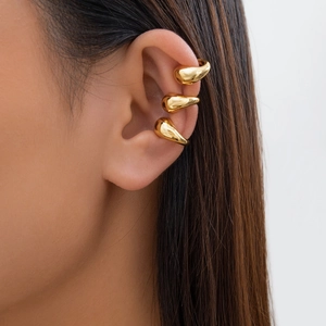 Close-up of three gold teardrop ear cuffs with polished finish worn on the ear
