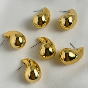 Macro view of three pairs of gold water drop earrings on a white silk background