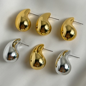 Detailed view of polished gold and silver waterdrop earrings on white leather texture