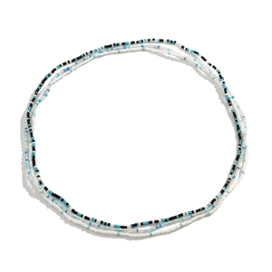 Detail van een gelaagde bohemian tailleketting met blauwe en witte kraaltjes op de achtergrond