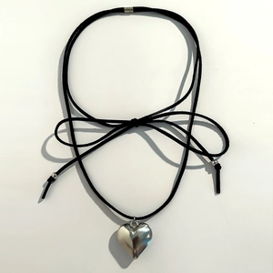 Detail of black cord choker with polished silver heart pendant and bow tie design