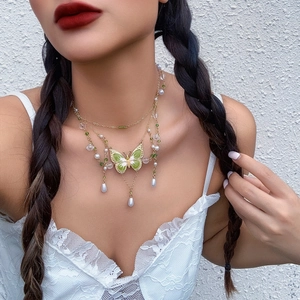 Detail einer Kette mit grünem Schmetterling und weißen Perlen im mehrlagigen Design