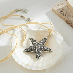 Detail of silver starfish pendant with textured finish on beige suede cord over seashell