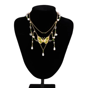 Details einer mehrlagigen Goldkette mit grünem Emaille-Schmetterling und weißen Perlen