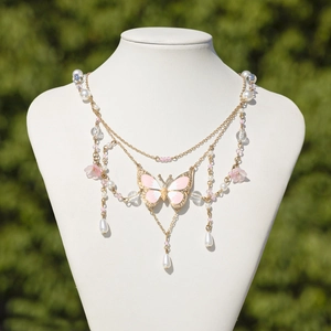 Detail einer mehrlagigen Goldkette mit rosa Emaille-Schmetterling und Perlenbesatz