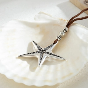 Detailed close-up of a silver starfish pendant on a brown cord over a white shell