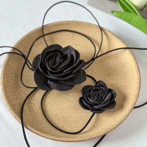 Macro shot of two black satin fabric rose chokers with thin ties on a ceramic plate
