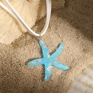 Blue starfish pendant necklace with iridescent sequins on a white cord over beach sand