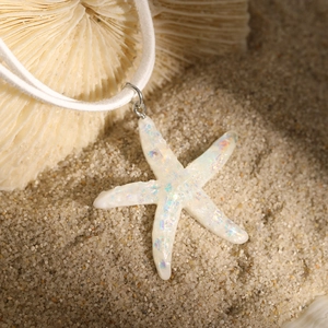 Macro shot of white iridescent starfish pendant with colorful sequins on beach sand