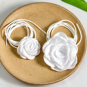 Macro detail of white satin camellia rose choker with long ribbon ties on a decorative plate