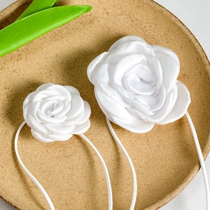 Detailed view of white satin rose chokers with elegant silk texture on a ceramic tray