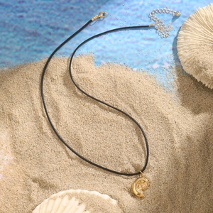 Macro detail of golden nautilus conch shell pendant on black cord over beach sand