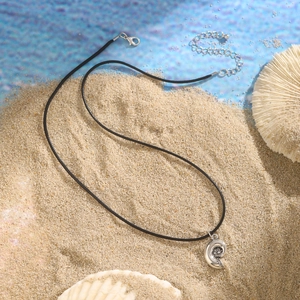 Macro detail of silver conch pendant with black wax rope on white beach sand