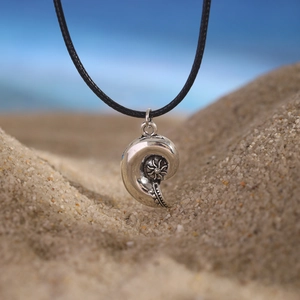 Close-up of bohemian silver sea shell pendant with floral relief on beach sand