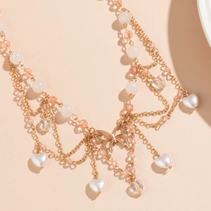 Detail einer mehrlagigen Goldkette mit Schmetterlingsanhänger, Perlenherzen und Perlen
