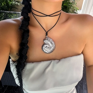 Detail of silver conch shell pendant on a black cord choker necklace worn by a model