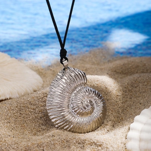 Detailed close-up of a silver nautilus shell pendant on sand with coral and water background