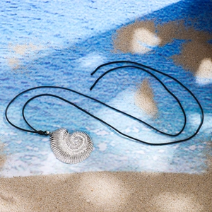 Detailed view of silver nautilus conch pendant with textured spiral on beach sand