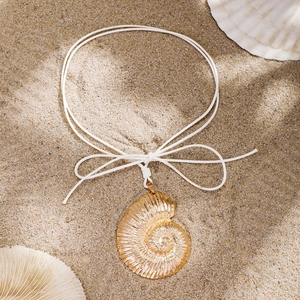 Detailed close-up of a golden nautilus pendant on white rope over a sandy beach