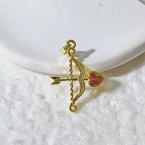 Close-up of golden Cupid's arrow pendant with pink heart gemstone and sparkling zircons