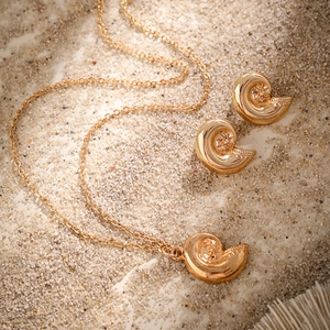 Detailed view of conch shell gold jewelry set on sand background with starfish embossing