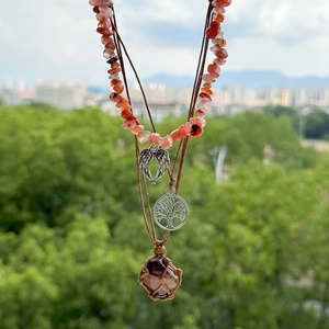 Detail einer Boho-Halskette mit Herzflügeln, Lebensbaum und braunem Steinanhänger