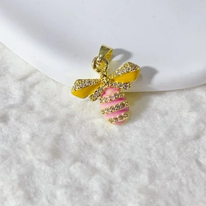 Gold bee pendant with yellow wings and pink crystal body on a white plush surface