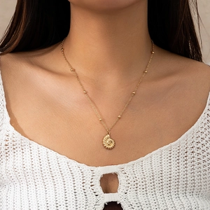 Close-up of golden nautilus shell pendant necklace on model with bohemian crochet top