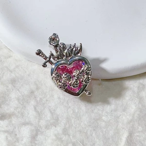 Macro-detail van een zilveren hartvormige hanger met roze zirkoon, zwaard en roos
