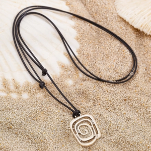 Detail of bohemian silver spiral pendant on sand with shells and coral decoration