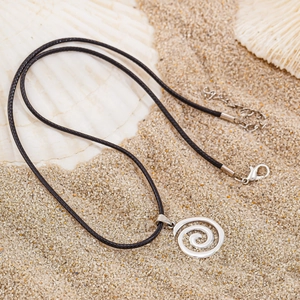 Detailed shot of silver conch spiral pendant on black cord over white beach sand