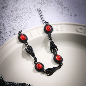 Detailed view of gothic black chain bracelet with red oval gems and bat accents