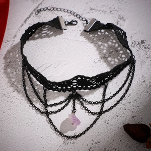 Détail d'un ras de cou en dentelle noire avec chaînes étagées et pendentif en pierre violette