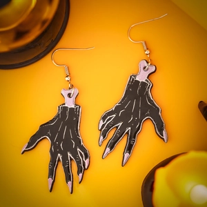 Close-up of gothic acrylic zombie hand earrings with purple details on orange background