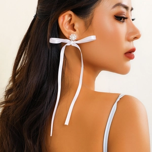 Detail of white silk ribbon bow earring with pearl flower stud worn by model