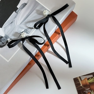 Detail of long black silk bow earrings with white faux pearl flower on vintage books