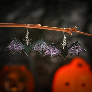 Detailed view of black and purple acrylic bat earrings hanging on a natural wooden branch