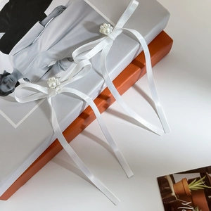 Close-up of white ribbon bow earrings with faux pearl cluster center on magazine