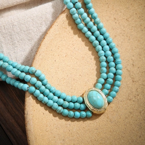 Gros plan d'un choker à trois rangs de perles turquoise avec pendentif ovale doré
