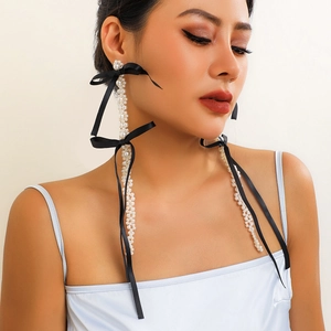 Detailed view of long pearl tassel earrings with black satin bow on model