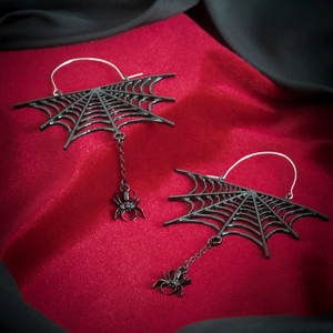 Close-up of gothic spider web earrings with dangling small spider charms on red velvet