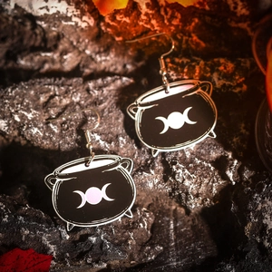 Macro detail of black cauldron acrylic earrings with triple moon symbol on dark rock