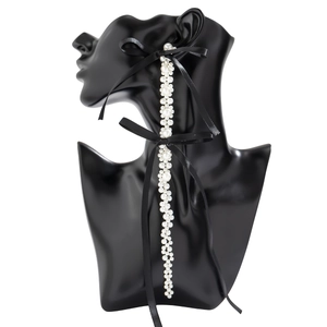 Close-up of long pearl drop earrings featuring black silk ribbon bows on a display
