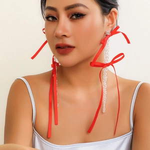 Close-up of long tassel earrings with clear beads and red ribbon bows on a model