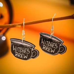 Close-up of black Witches Brew cauldron acrylic earrings hanging on a dry branch