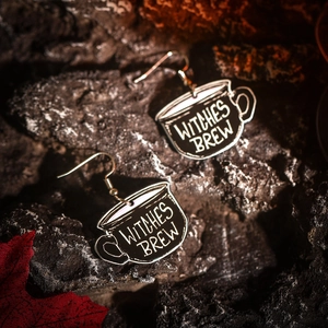 Detailed shot of black Witches Brew acrylic earrings on autumn leaves and dark background