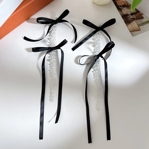 Detailed view of long crystal tassel earrings with elegant black satin bows on white backdrop