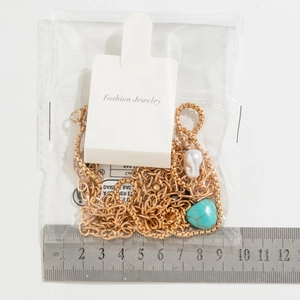 Détail du collier doré multicouche avec pendentif cœur turquoise et perle sur carte
