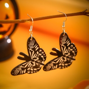 Close-up of butterfly earrings with skull patterns hanging on a branch for Halloween decor
